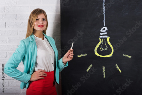 An attractive young woman with chalk at the blackboard with Idea Bulb Concept photo