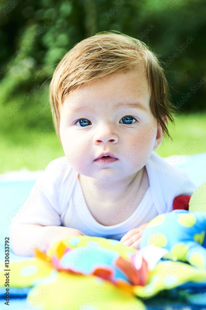 Newborn girl with blue eyes in the beautiful park outdoors, lies on a blue blanket with some toys and looking around. Newborn girl with blue eyes in the beautiful park outdoors, lies on a blue blanket with some toys and looking around.