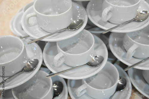 White cups and saucers with spoons are on each other in the shape of a pyramid