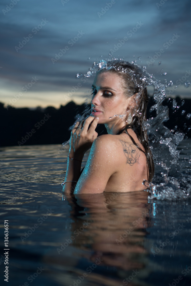 Fototapeta premium Portrait of sensual woman alone in infinity swimming pool over beautiful tropical and sunset sky background