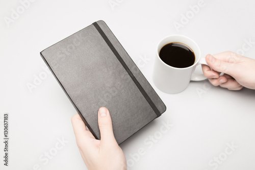 Hand is holding the notebook and coffee cup