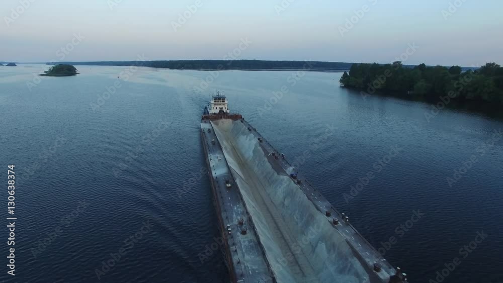 Empty cargo transport ship sailing on a wide river. Summer dawn. The camera moves in the air near from the ship. The island in the middle of the river. Freight on the river. Aerial view. Empty cargo transport ship sailing on a wide river. Summer dawn. The camera moves in the air near from the ship. The island in the middle of the river. Freight on the river. Aerial view.