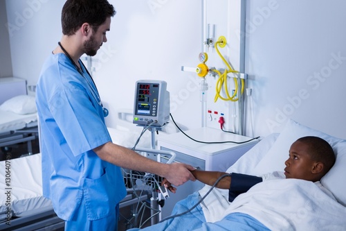 Male nurse checking patient blood pressure in ward
