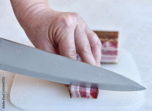 Hands of a woman cutting bacon in small pieces. Selective focus.