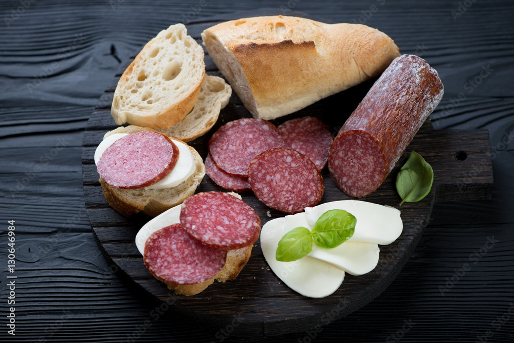 Baguette with salami and mozzarella over black wooden surface Baguette with salami and mozzarella over black wooden surface