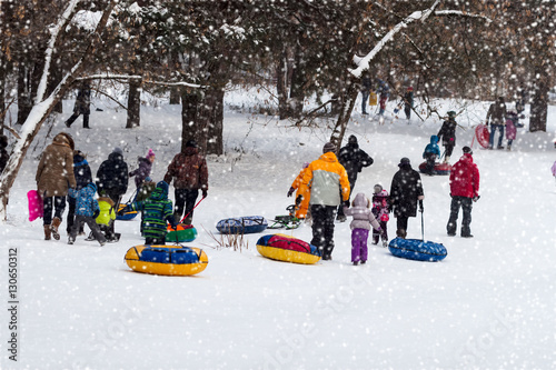 Children with parents are sleding from the hill in one of snowy park, winter leisure, active lifestyles, tobogganing, Christmas. Selective focus.