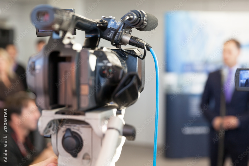 Video camera in focus, blurred spokesman in background Video camera in focus, blurred spokesman in background