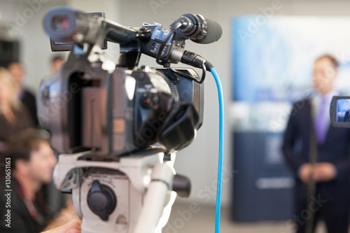Video camera in focus, blurred spokesman in background