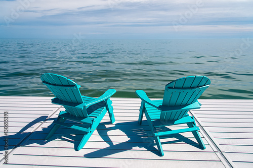 Muskoka or Adirondack Chairs on a dock overlooking the water with blue sky