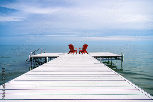 Red Adirondack or Muskoka Chairs on the dock overlooking the water at the cottage photo