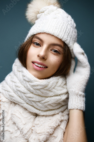 Beautiful girl in a white knitted hat with fur pompom. Model with gentle nude make-up. Cozy winter picture. Beautiful face.