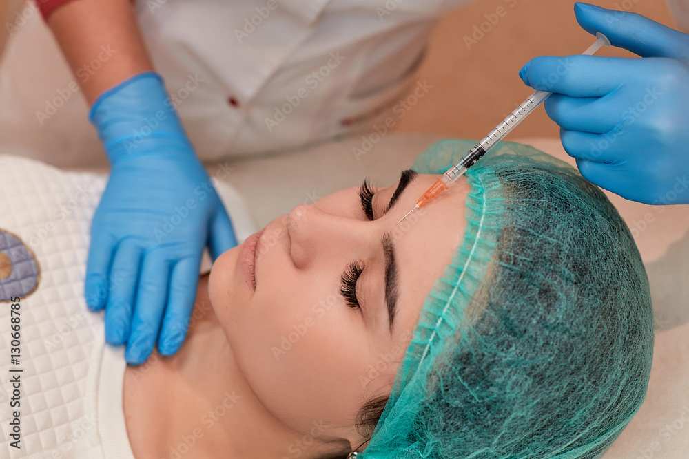 Beautiful young woman is caring of her skin at beautician office. She is sitting and getting injection. Her eyes are closed with tranquility