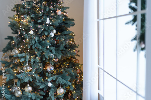 Christmas tree with decorations and lights in living room near the window