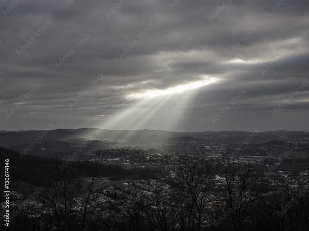 Sun breaking through clouds, shining on rural town, black and white