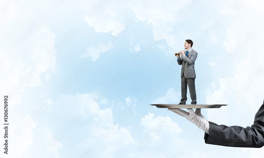 Businessman on metal tray playing fife against blue sky background Businessman on metal tray playing fife against blue sky background