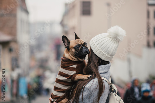 Street outdoors of beautiful and fashinable brunette woman with her adorable French bulldog. 