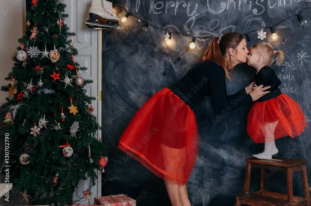 Happy Mother and daughter standing near Christmas tree  and black board. kissing and hugging each other