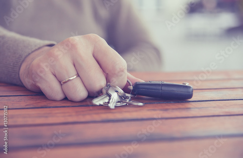  Hands of man holding the car keys with black wallet on wooden table