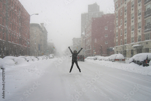 Woman dressed in cold gear jumping up in the middle of an empty street during a snow storm in New York City