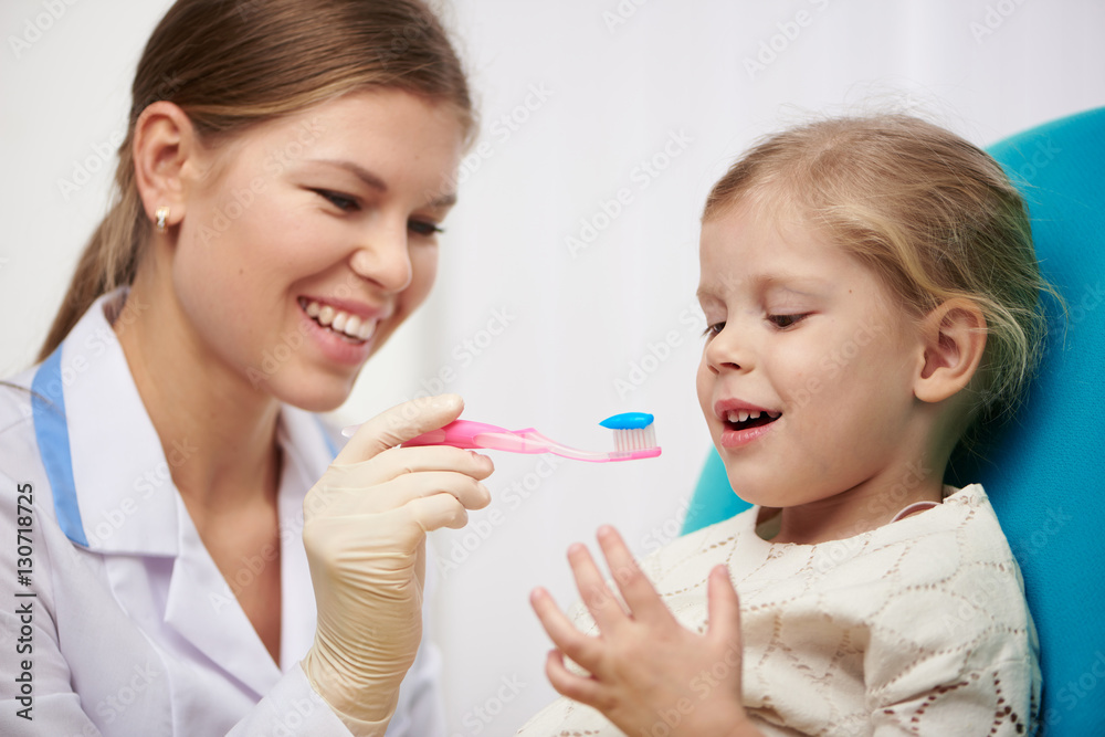 Female hygienist teaching little girl to brush teeth in dental clinic. Dental care concept. Female hygienist teaching little girl to brush teeth in dental clinic. Dental care concept.