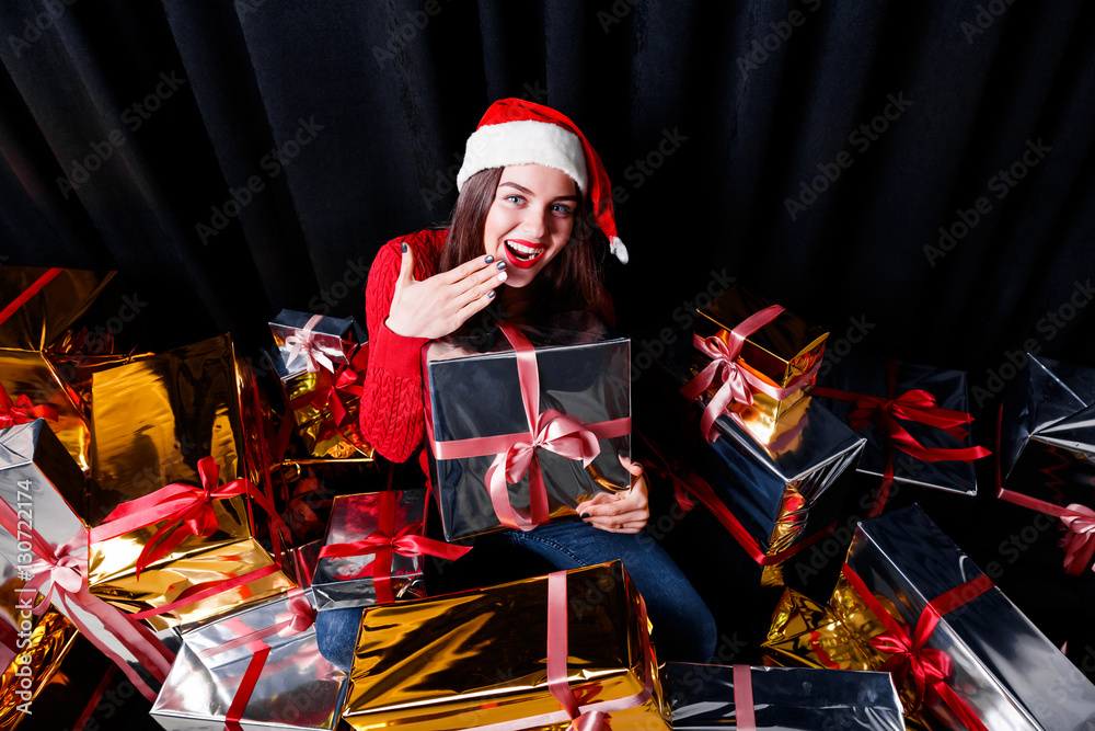 Happy woman in Santa hat with many Christmas gifts