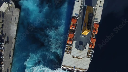 Flying over big ferryboat. The ferry turns and walks away from the pier. The camera rises high into the sky above the ship. Foamy track behind the stern. Aerial view.