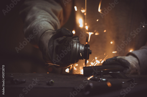 Close up of worker cutting a piece of metal in a dark industrial workshop, generating sparks