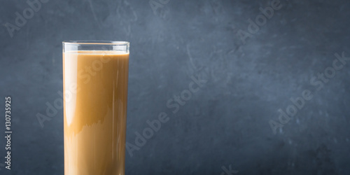 Long glass with coffee drink and cream on dark blue and black textured background. Banner image