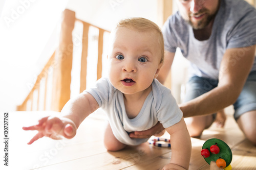 Father supporting crawling baby at home photo