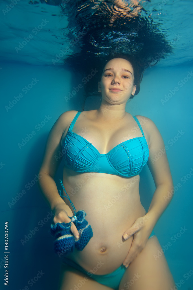 Pregnant girl in bikini underwater on a blue background holding baby shoes.  Portrait. Vertical view Stock 写真 | Adobe Stock