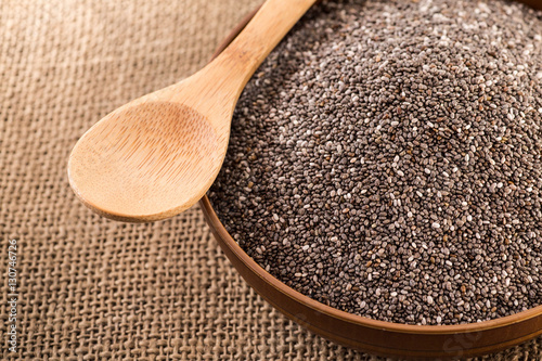 Wooden bowl full with chia seeds and a spoon next to it on sack cloth backgro...