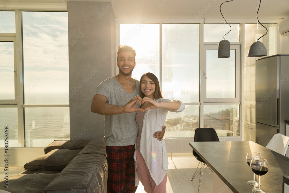 Young Mixed Race Couple Apartment Panoramic Window Sea View Morning, Happy Hispanic Man Asian Woman Embracing Making Heart Shape Modern Kitchen