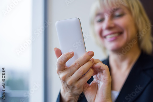 Woman holding white mobile phone and smiling. Closeup.