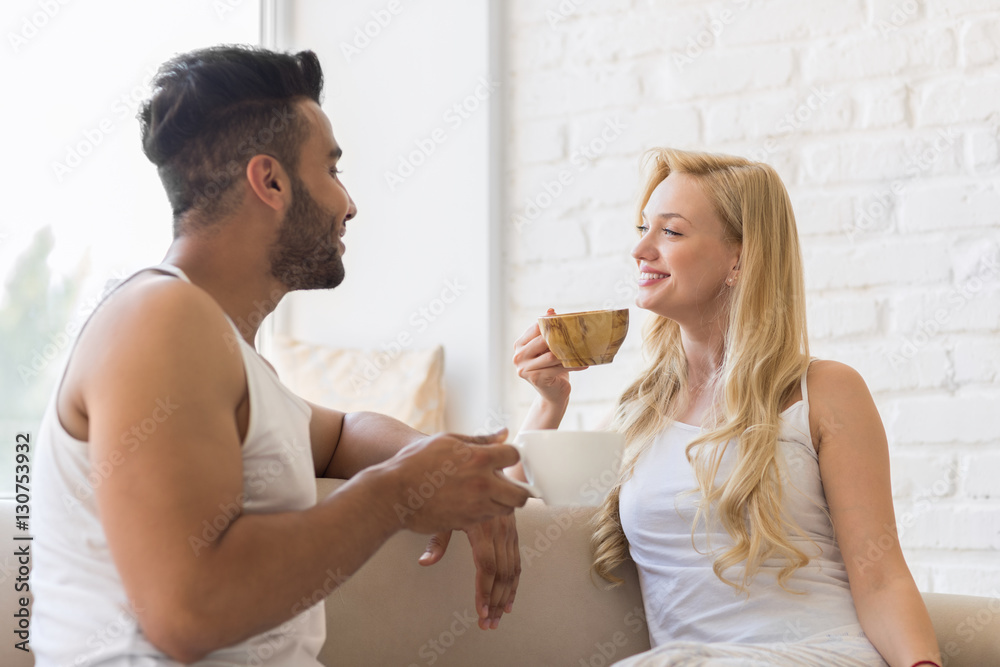 Young Beautiful Couple Sit On Coach Near Window, Drink Morning Coffee Cup, Happy Smile Hispanic Man And Woman Lovers Young Beautiful Couple Sit On Coach Near Window, Drink Morning Coffee Cup, Happy Smile Hispanic Man And Woman Lovers