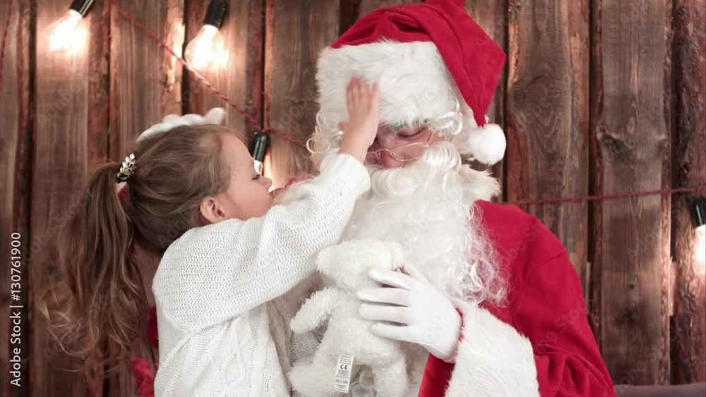 Little girl with teddy bear checking Santa's beard Little girl with teddy bear checking Santa's beard