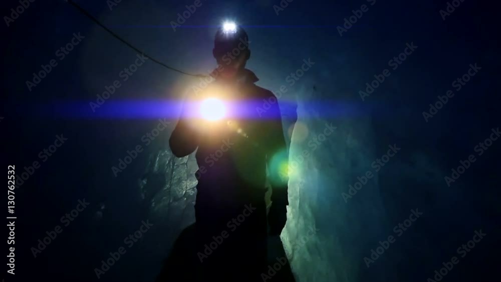 walking scientist holding flashlight exploring dark ice cave. blue light beaming  background.