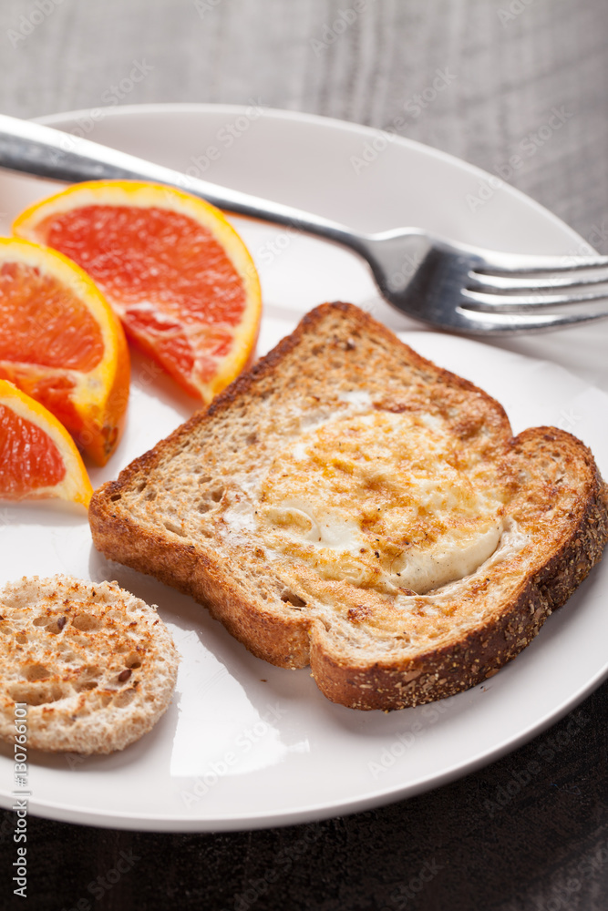 Toad in a hole egg breakfast with Cara Cara oranges on a white plate and dark background