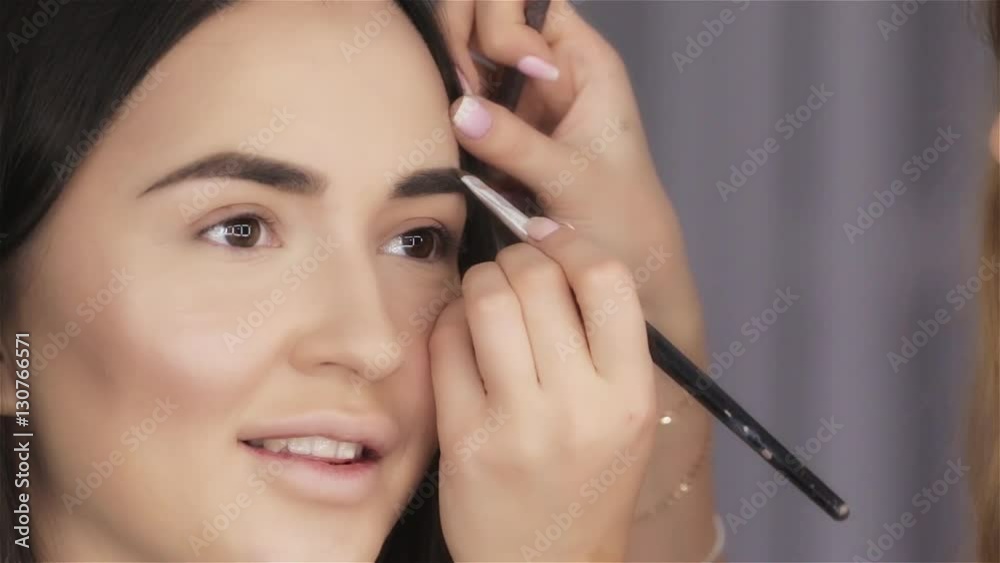 Make up artist paints eyebrow of beautiful brunette young woman close-up Make up artist paints eyebrow of beautiful brunette young woman close-up