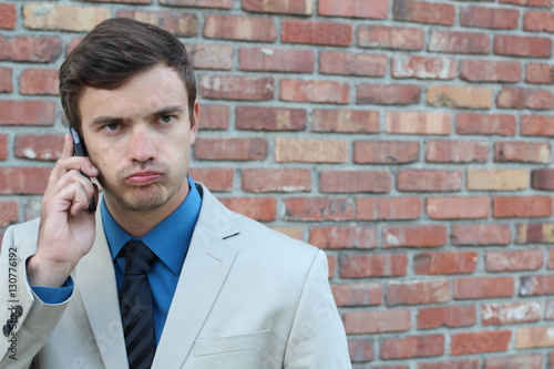 Desperate young brown-haired businessman get bad news heavy problems, faces challenges snort while talking on the mobile phone on brick wall isolated background