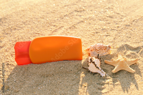 Sunscreen cream, sea shells and starfish on sand, close up view