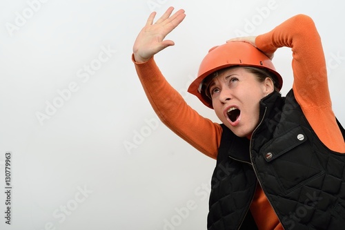 The woman construction in a helmet is frightened danger a threatening from the top and defended stretched arm