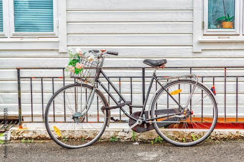 Parked vintage bicycle with basket with flat forward tire at white wooden house background. Norway, Bergen. © Feel good studio