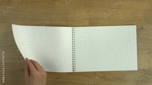 Hand flipping through a blank spiral notepad, all empty white sheets of paper, you can add your own text or drawings