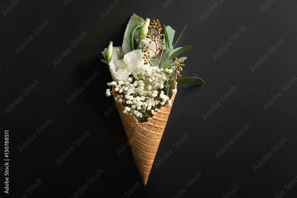 Waffle cone with composition of flowers and branches on dark background