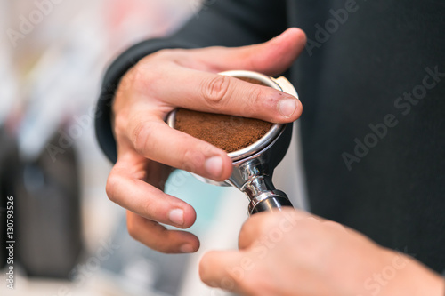 Barista using a tamper to press ground coffee  