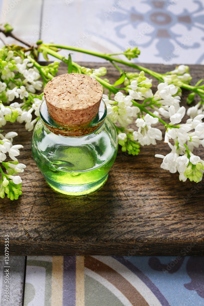 Bottle of green essential oil and lilac flowers