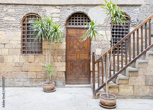 Facade of a historic house with wooden closed door and two window with interleaved wooden grid and stair with wooden handrail, Medieval Cairo, Egypt photo
