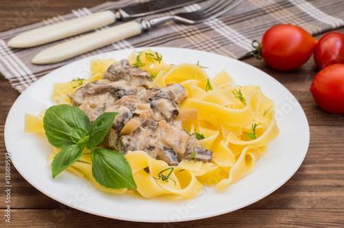 Fettuccine pasta in a creamy sauce with mushrooms on  plate   wooden table. Horizontal top view. Close-up photo