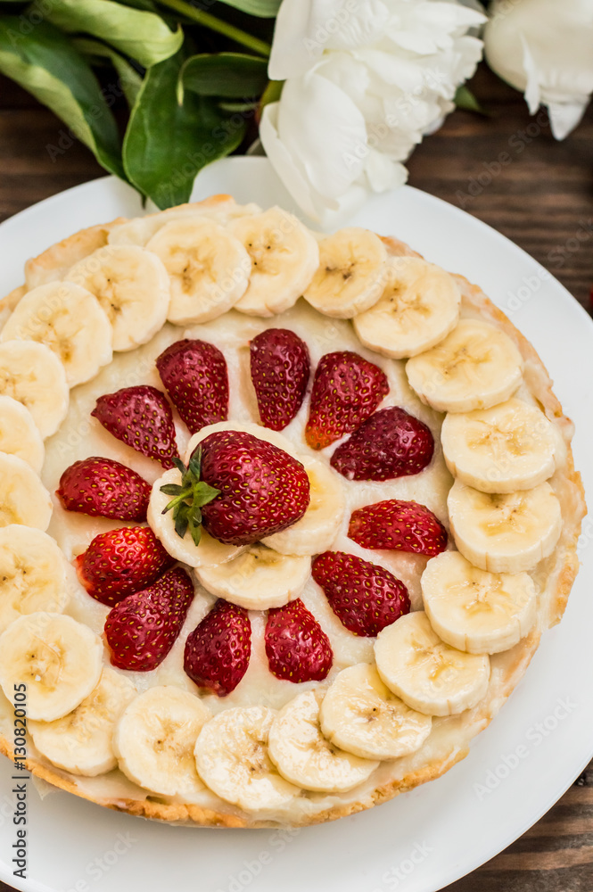 Tart with strawberries, bananas and whipped cream on a background of flowers. Top view. Close-up