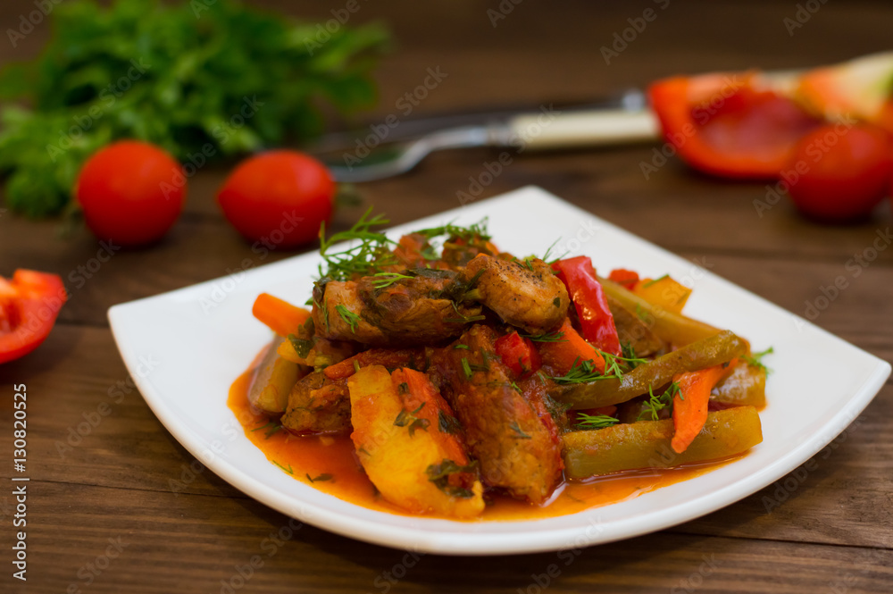 Stew with potatoes, carrots, pickles, tomatoes and hot peppers. Azu by Tartarian on a white square plate. Wooden rustic background. Top view. Close-up